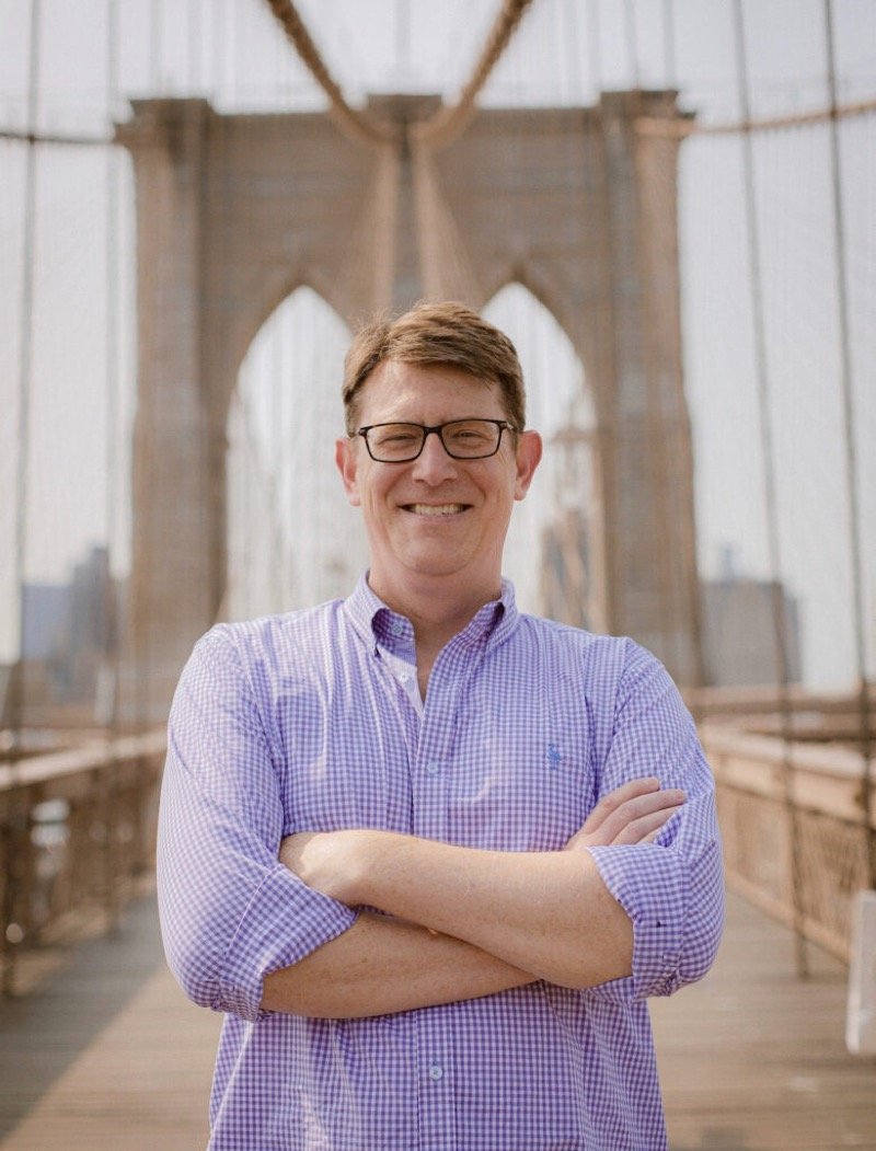 Will Kimball, arms folded, on a bridge with his trombone